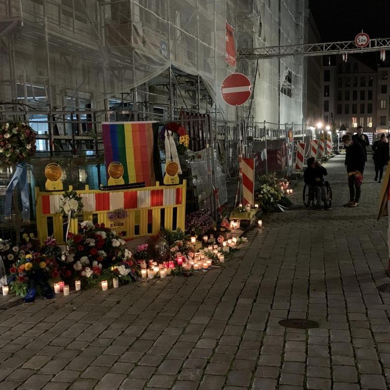 An der Straßenecke an der Schlossstraße, mitten in der Dresdener Innenstadt zwischen Kulturpalast und Residenzschloss, wo ein schwules Paar angegriffen und einer der beiden Männer getötet wurde, erinnern Blumenkränze und Kerzen an die Opfer. Inzwischen hat jemand dort auch eine Regenbogenfahne befestigt.