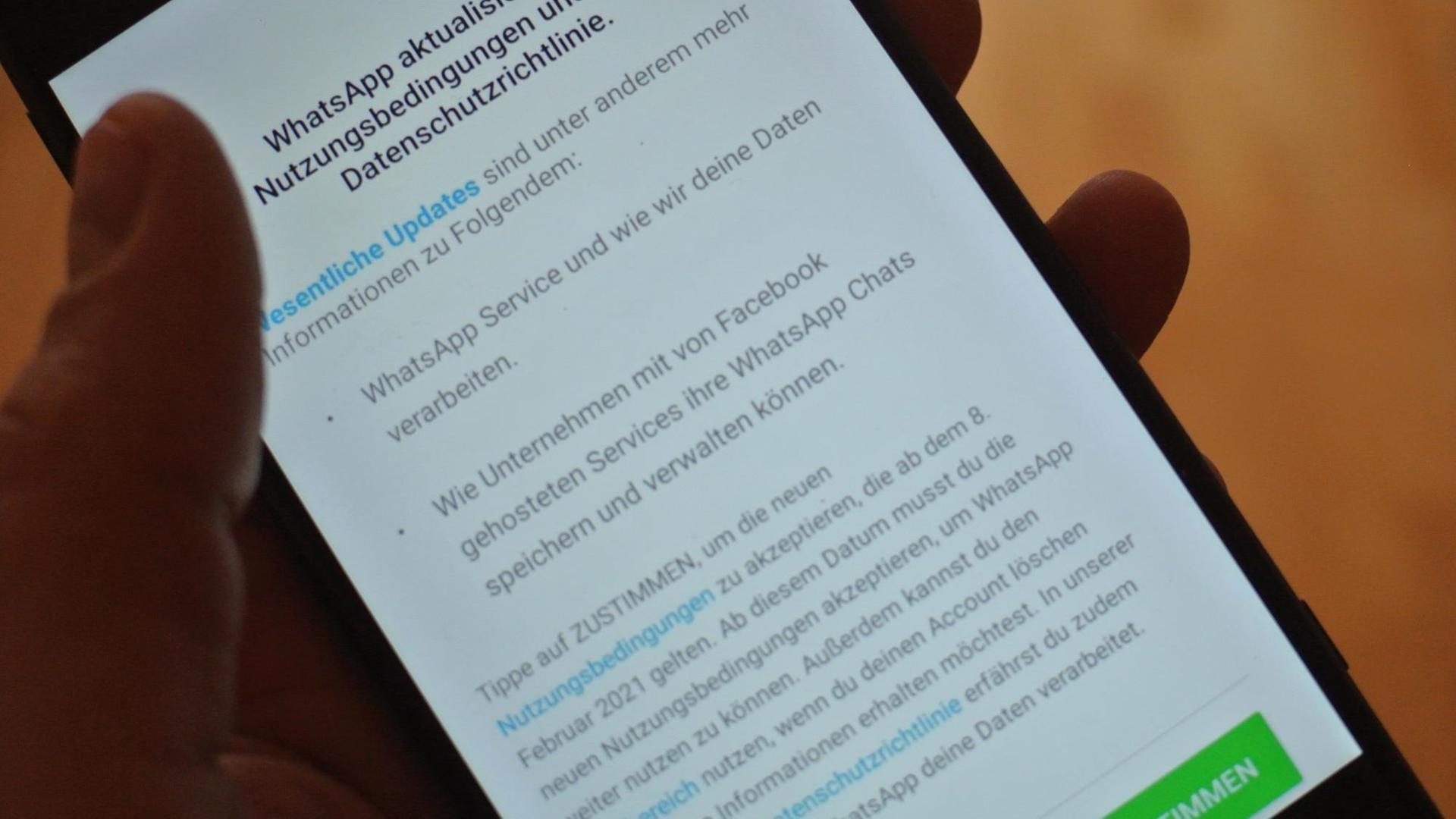 Eine Hand hält ein Smartphone, wo die neuen Nutzungsbedingungen von WhatsApp zu sehen sind Eine Hand hält ein Smartphone, wo die neuen Nutzungsbedingungen von WhatsApp zu sehen sind