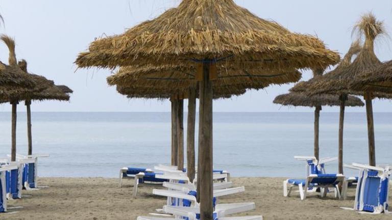 Ein Strand mit Sonnen-Schirmen auf der spanischen Insel Mallorca.