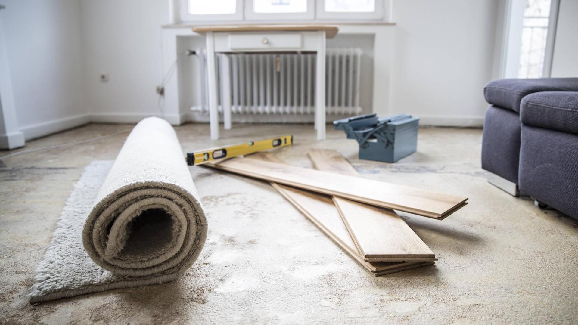 Ein Raum, der renoviert wird. Holzlatten, Teppiche und Arbeitsmaterialien von Handwerkern liegen auf dem Boden.