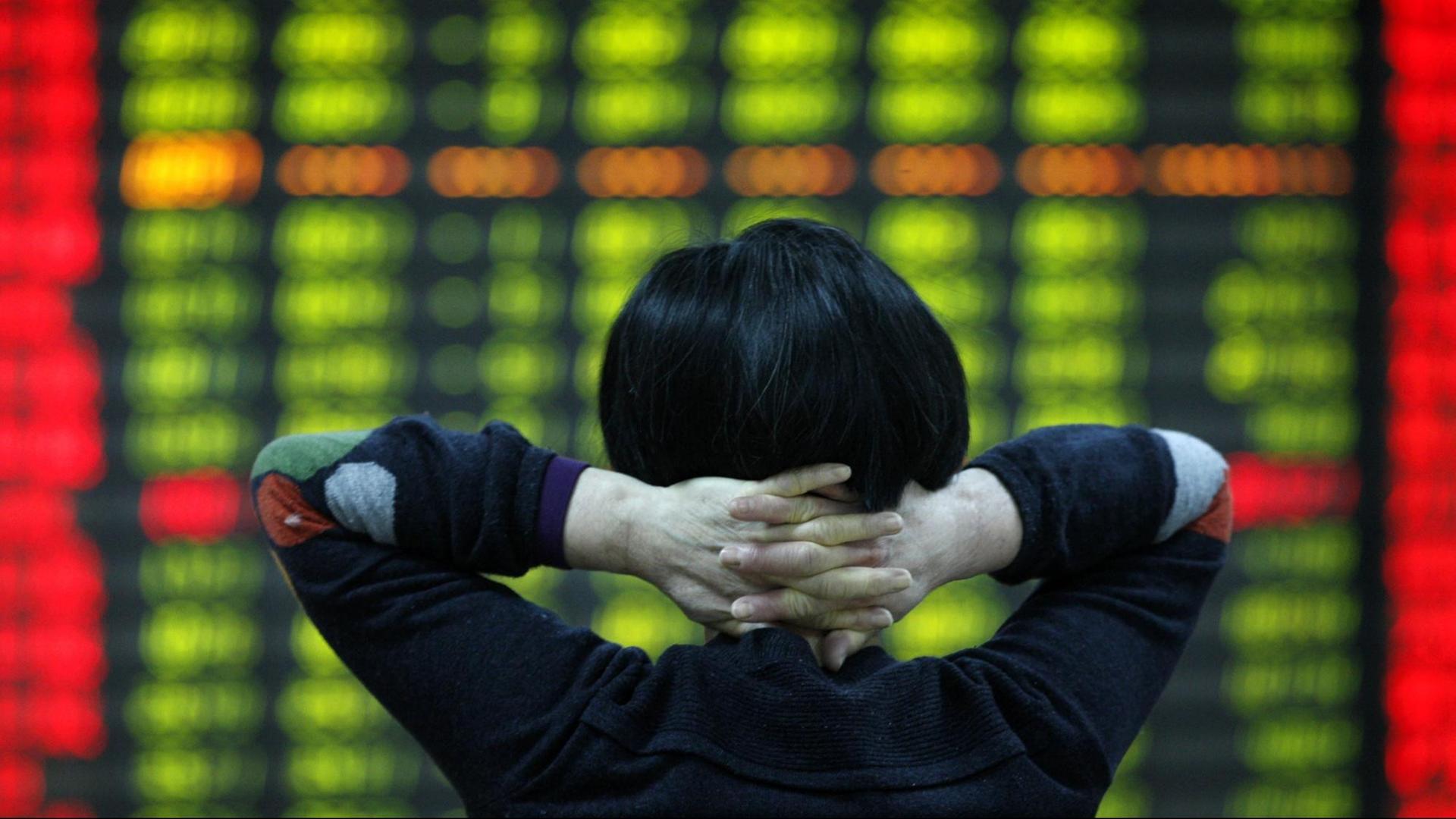 Ein chinesischer Investor steht vor einer Anzeigetafel für Aktienkurse.