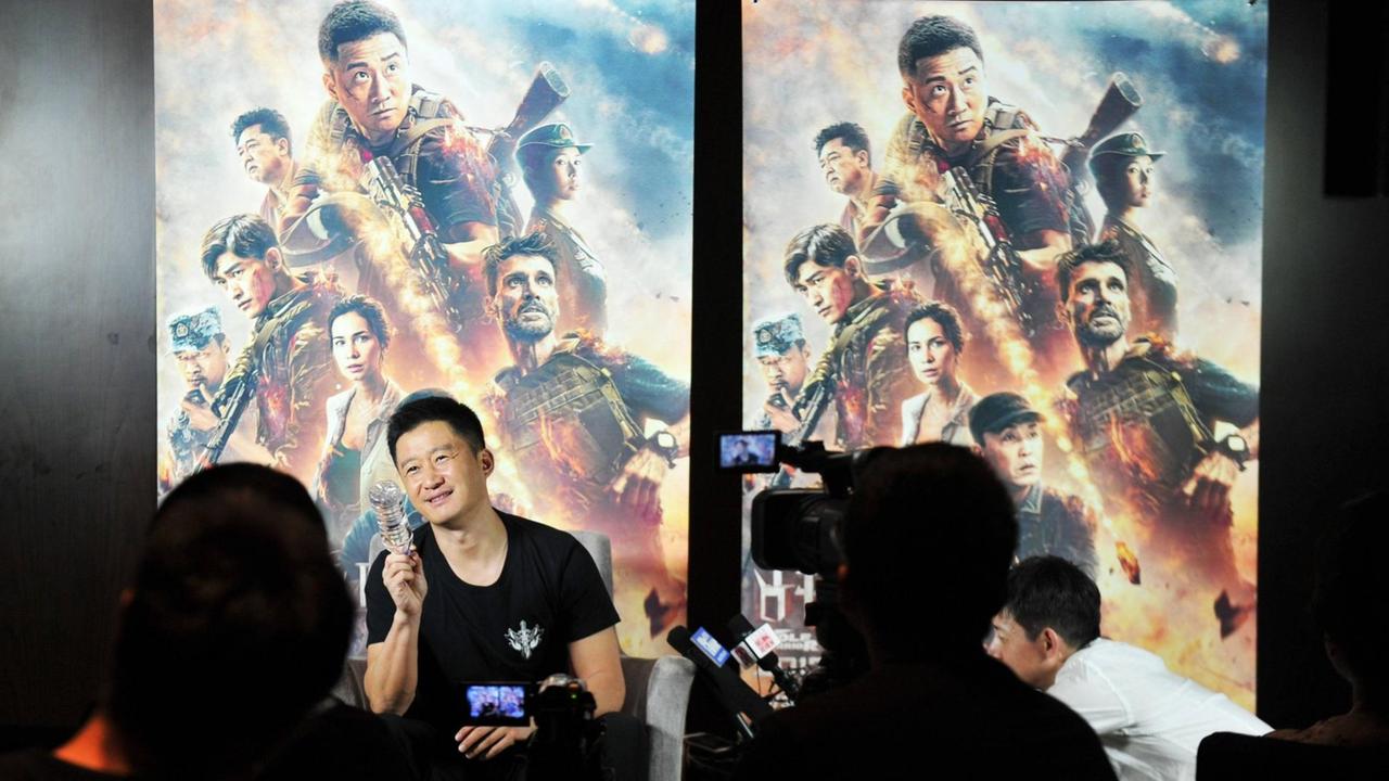 Wu Jing vor Filmplakaten zu Wolf Warrior 2. Im Vordergrund Journalisten mit Kameras und Mikrofonen. Wu Jing vor Filmplakaten zu Wolf Warrior 2. Im Vordergrund Journalisten mit Kameras und Mikrofonen.