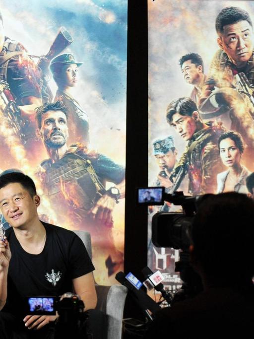 Wu Jing vor Filmplakaten zu Wolf Warrior 2. Im Vordergrund Journalisten mit Kameras und Mikrofonen.
