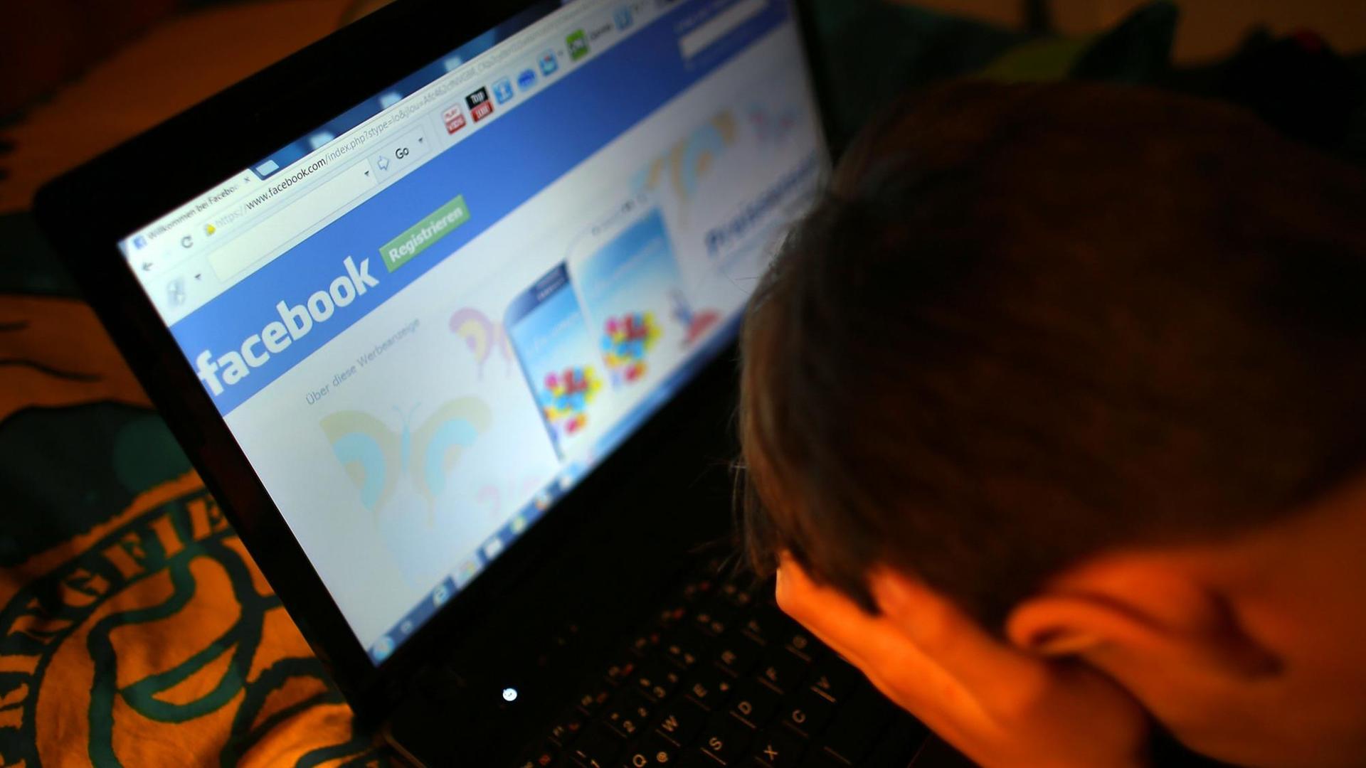 Ein Mensch sitzt mit in den Händen vergrabenem Gesicht vor einem Bildschirm, auf der Facebook angezeigt wird.