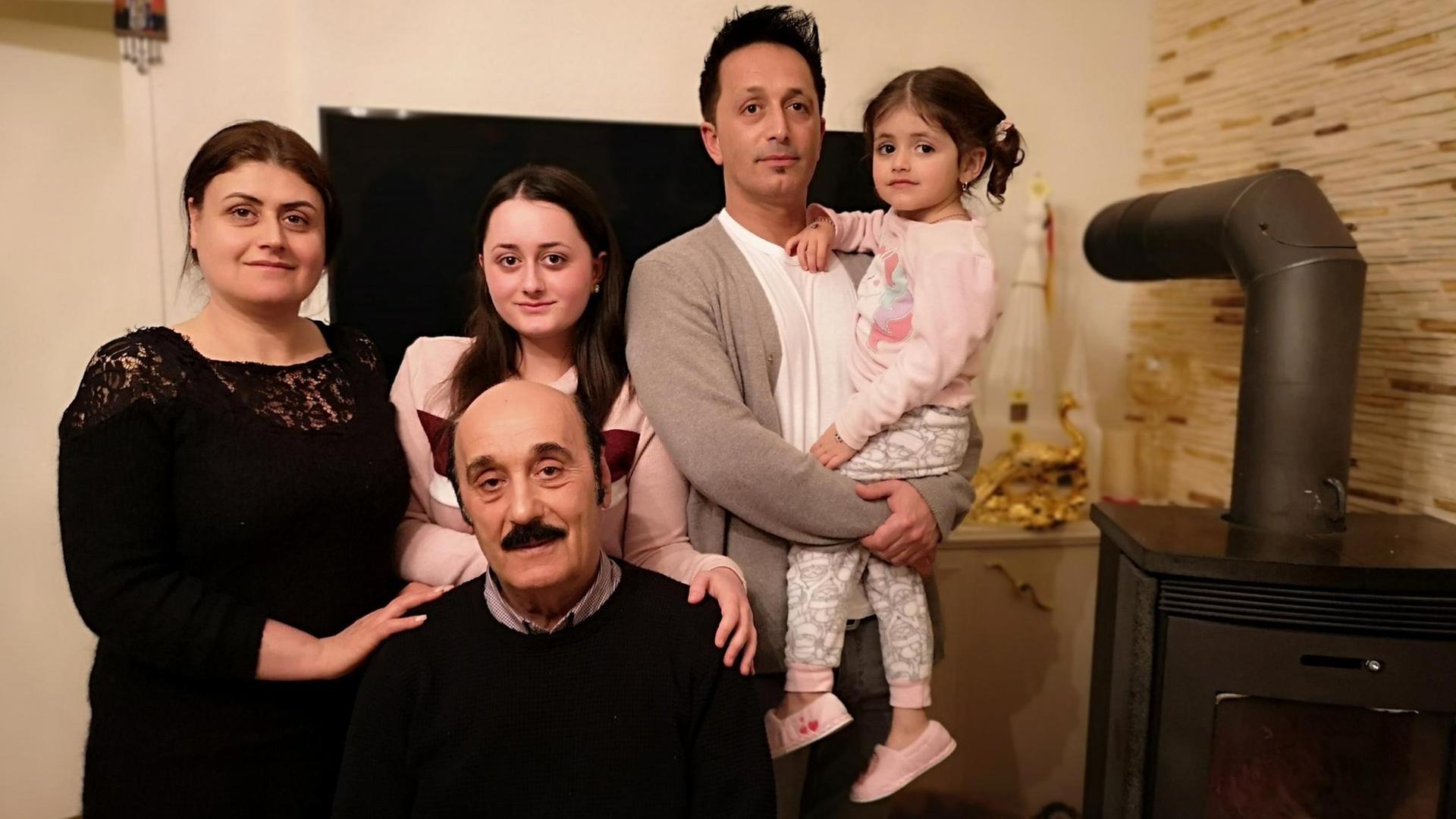 Das Foto zeigt die jesidische Familie Kizilyel in ihrem Wohnzimmer: Im Bildvordergrund sitzt Vater Behcet Kizilyel, dahinter rechts im Bild sein Sohn Salhattin sowie sein Enkelkind und zwei weibliche Familienmitglieder. Kizilyel lebt seit 50 Jahren in Celle.