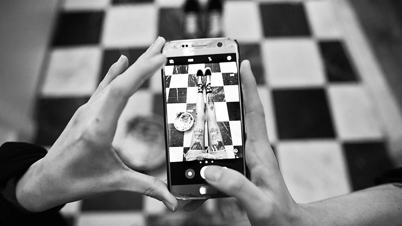 Eine Frau fotografiert mit einem Handy ihre ausgestreckten Beine. Eine Frau fotografiert mit einem Handy ihre ausgestreckten Beine.