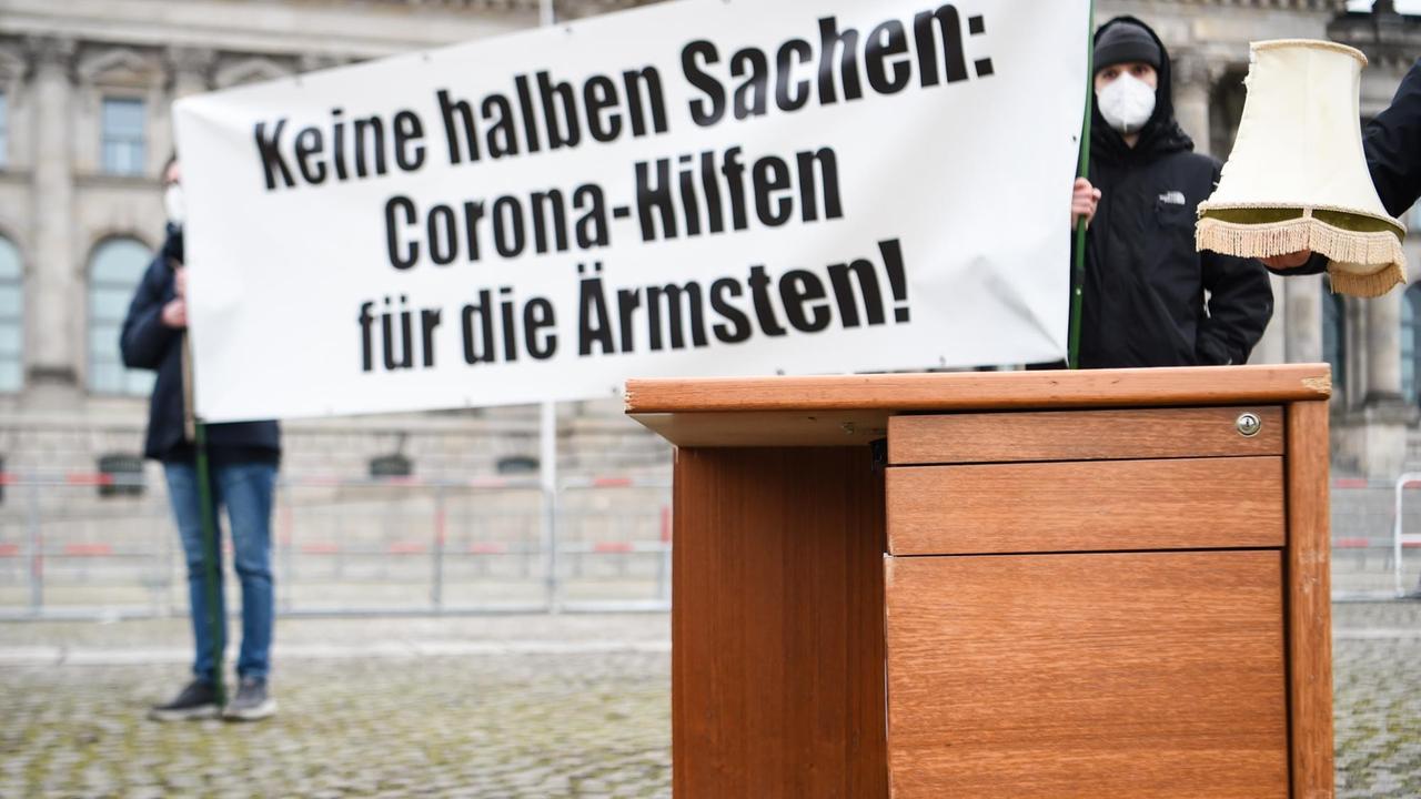 Ein halber Tisch steht vor Demonstranten und Demonstrantinnen, die ein Schild hochhalten. Vor dem Deutschen Bundestag demonstrieren Personen der Aktion «Keine halben Sachen: Corona-Hilfen für die Ärmsten» für mehr Corona-Hilfen 