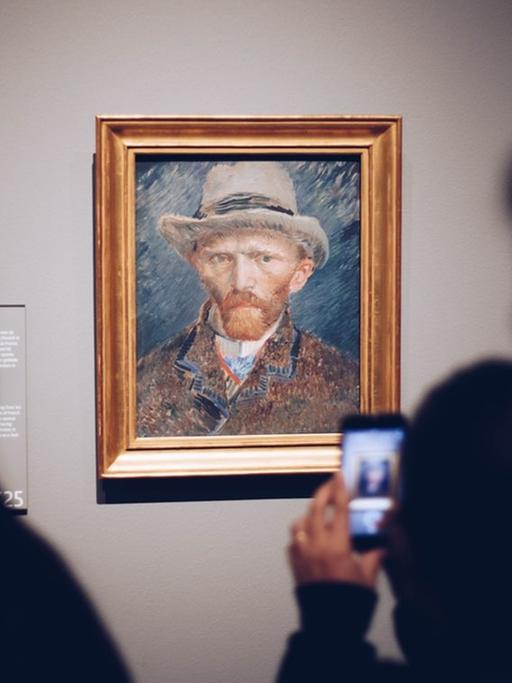 Ein Mann im Rijksmuseum in Amsterdam macht mit seinem Handy ein Foto von van Goghs Selbstporträt.