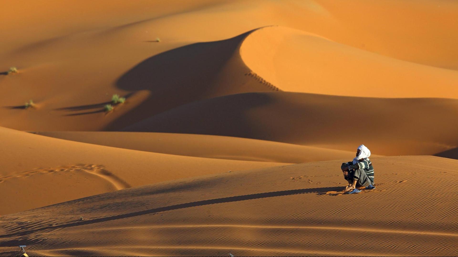 Berber sitzt im Wuestensand, Marokko, Merzouga.