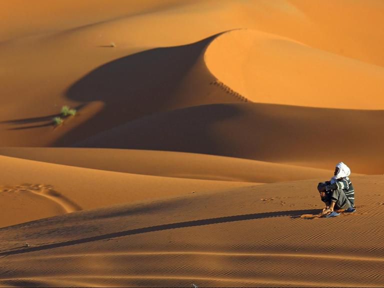Berber sitzt im Wuestensand, Marokko, Merzouga.
