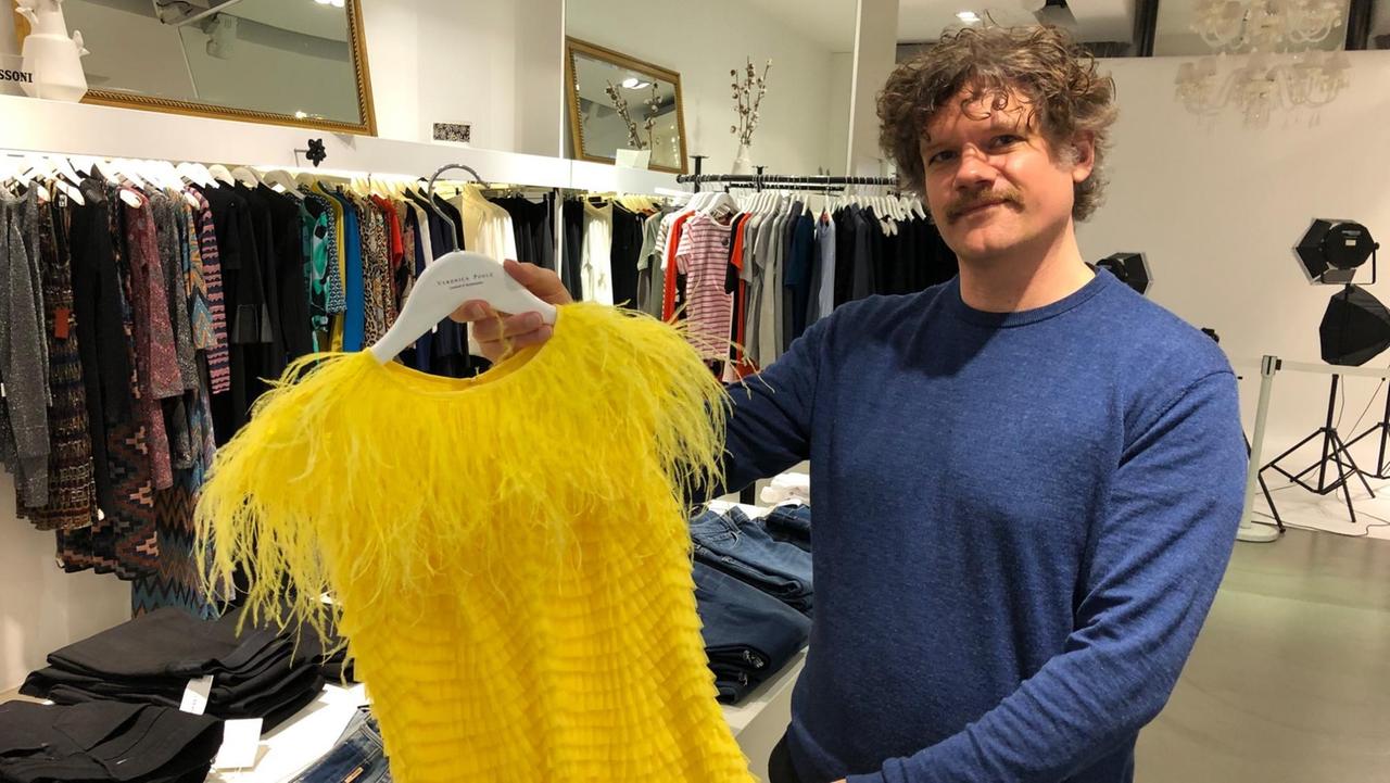 Arik Tremmel hält ein gelbes Kleid auf einem Bügel in der Hand. Arik Tremmel hält ein gelbes Kleid auf einem Bügel in der Hand.