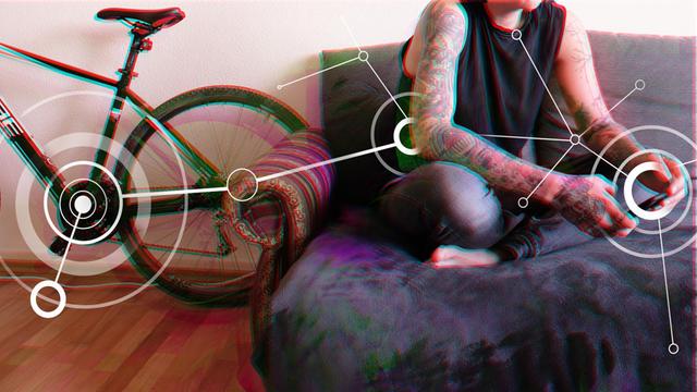 Ein tätowierte Frau sitzt auf einem Sofa links von ihr steht ein Rennrad.