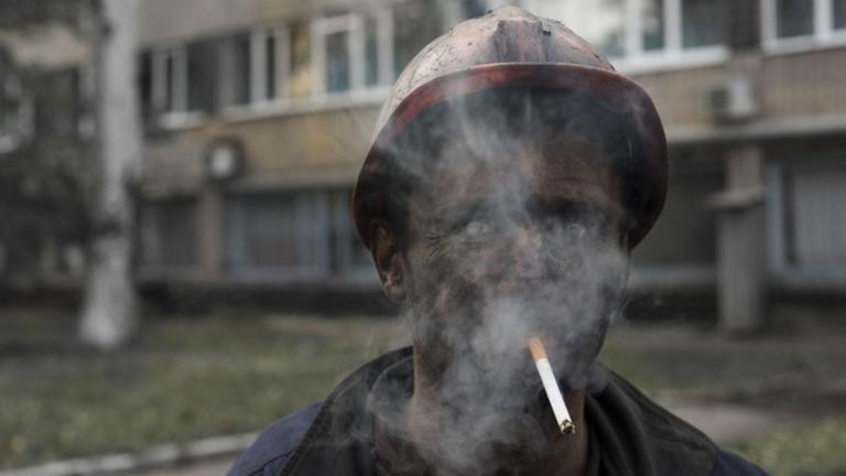 Ein ukrainischer Bergarbeiter bläst dichten Zigarettenrauch aus, durch den man kaum noch sein Gesicht erkennt.