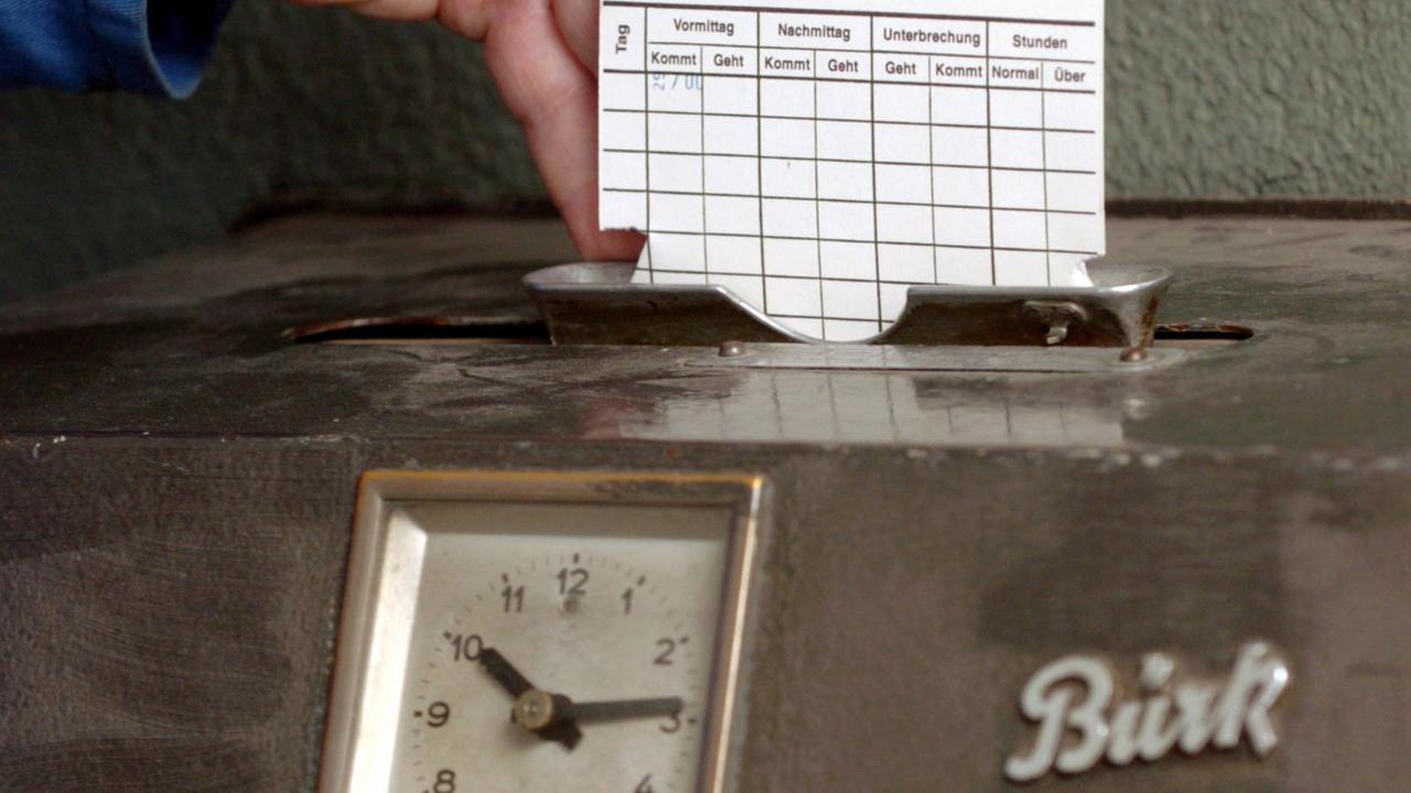 Eine Hand steckt eine Karte in ein Arbeitszeiterfassungsgerät.
