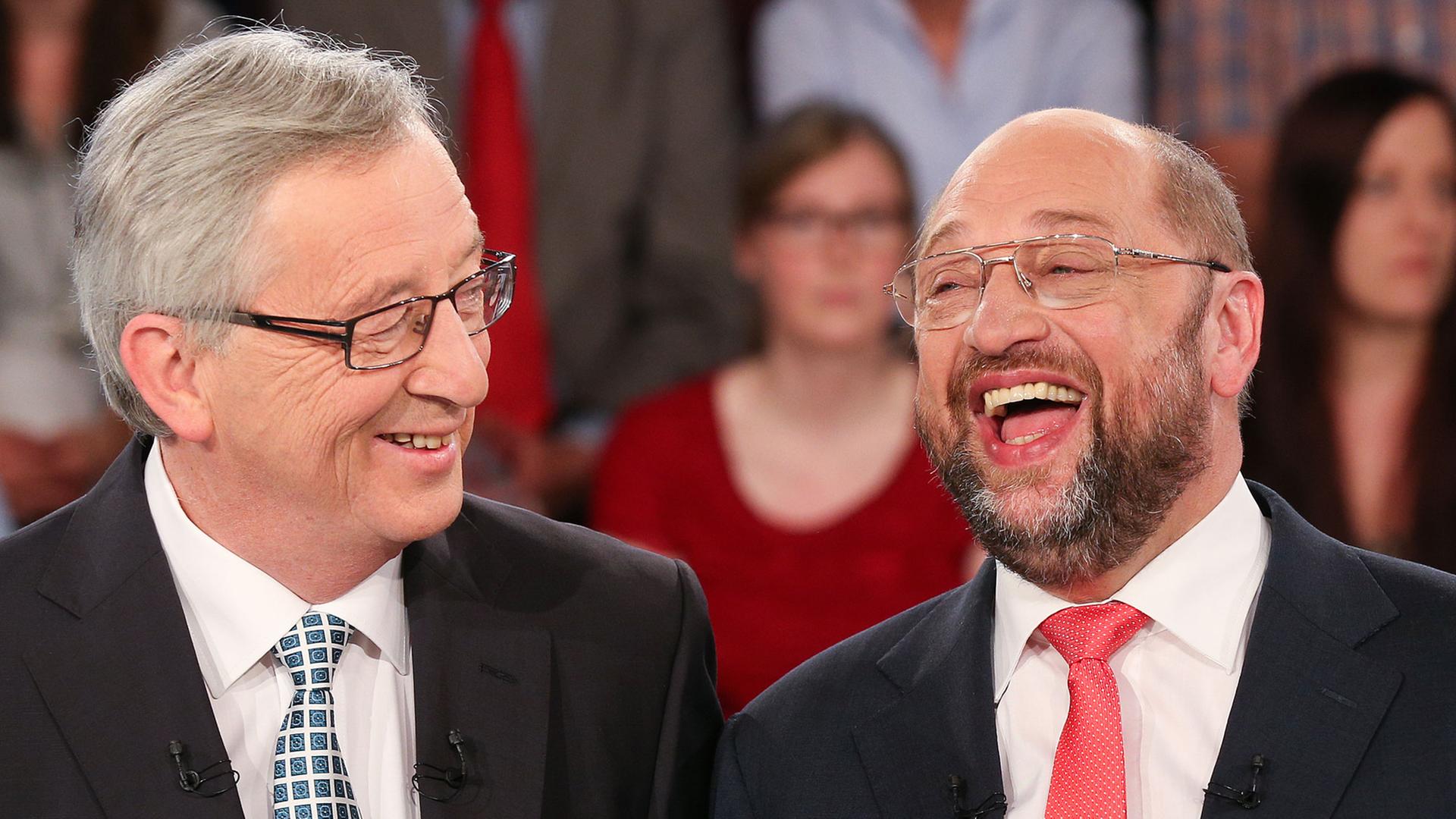 Jean-Claude Juncker und Martin Schulz lachen im Fernsehstudio miteinander