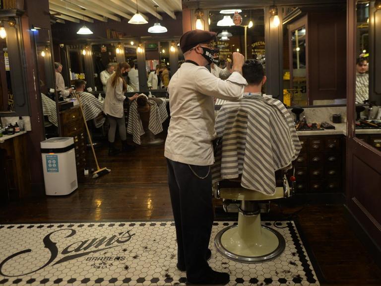 Ein Friseur mit Maske schneidet einem Kunden die Haare.