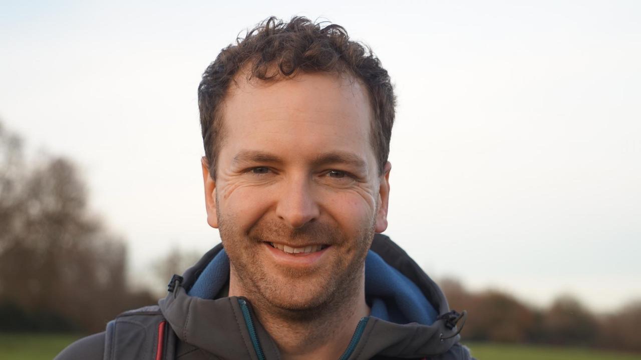 Patrick McKearney lächelt in die Kamera, im Hintergrund sind Bäume und eine Wiese zu sehen Patrick McKearney lächelt in die Kamera, im Hintergrund sind Bäume und eine Wiese zu sehen