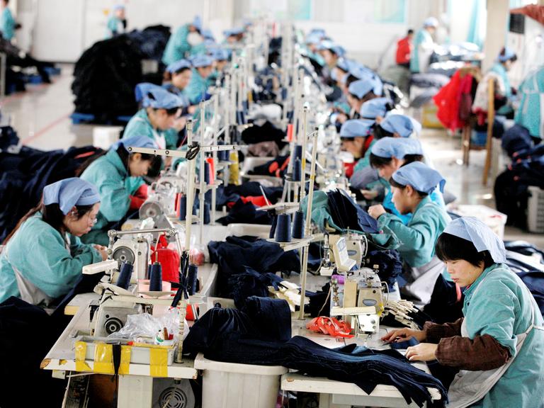 Etwa 20 Arbeiterinnen konzentrieren sich an einem langen Tisch auf ihre Nähmaschinen.