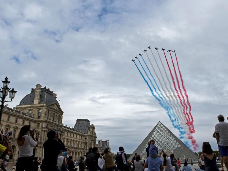 Menschen schauen sich die Düsenjet-Performance am Nationalfeiertag auf dem Platz des Louvre an.