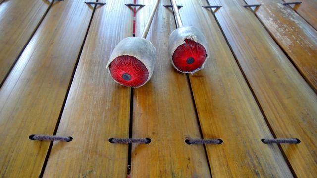 Weiß umwickelte Schlägel mit rotem Kern liegen auf den hölzernen Röhren eines Xylofons.