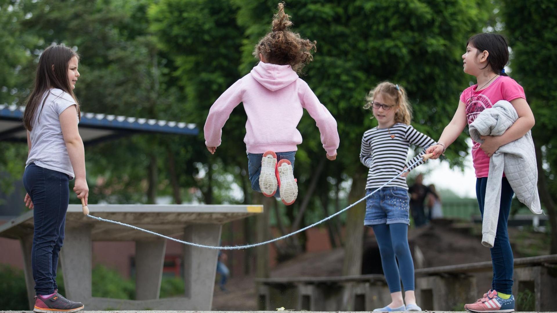 Auf dem Pausenhof einer Grundschule springen Schüler Seil.