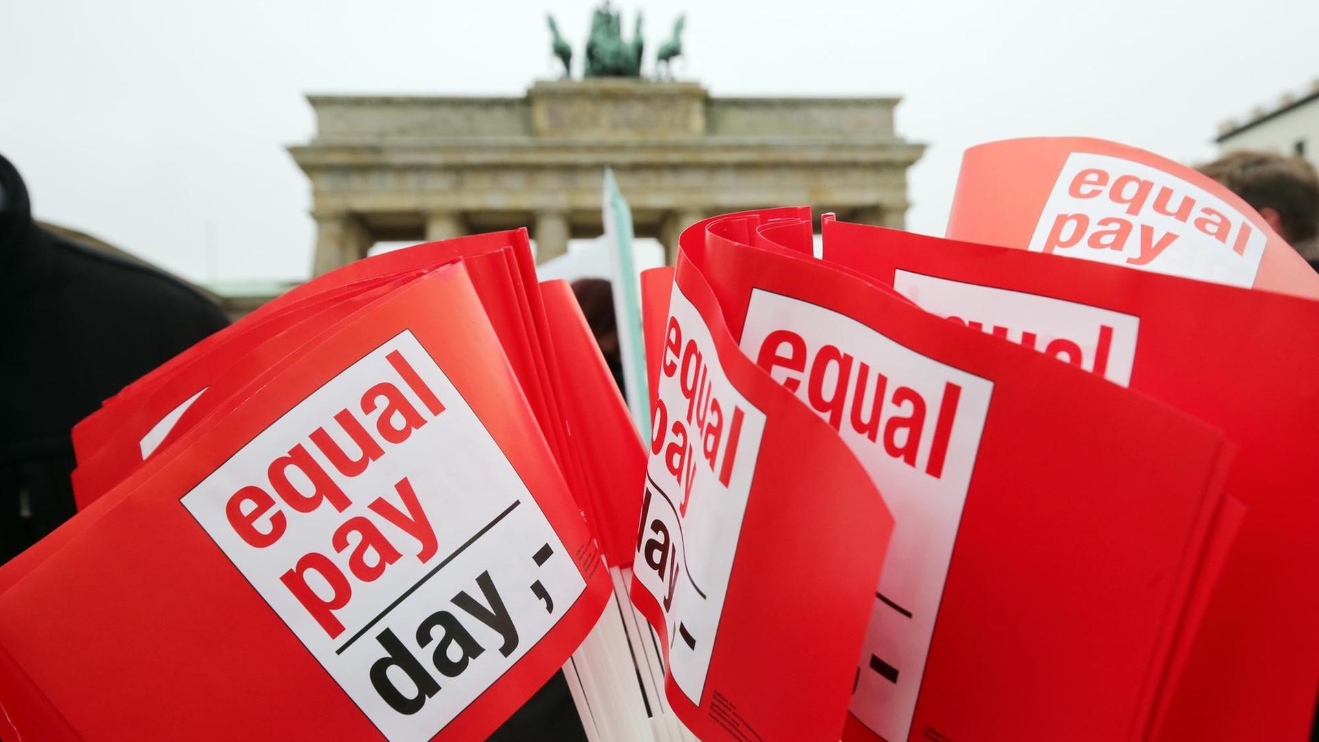 Rote Winkfähnchen mit der Aufschrift "Equal Pay Day", im Hintergrund das Brandenburger Tor in Berlin. Rote Winkfähnchen mit der Aufschrift "Equal Pay Day", im Hintergrund das Brandenburger Tor in Berlin.