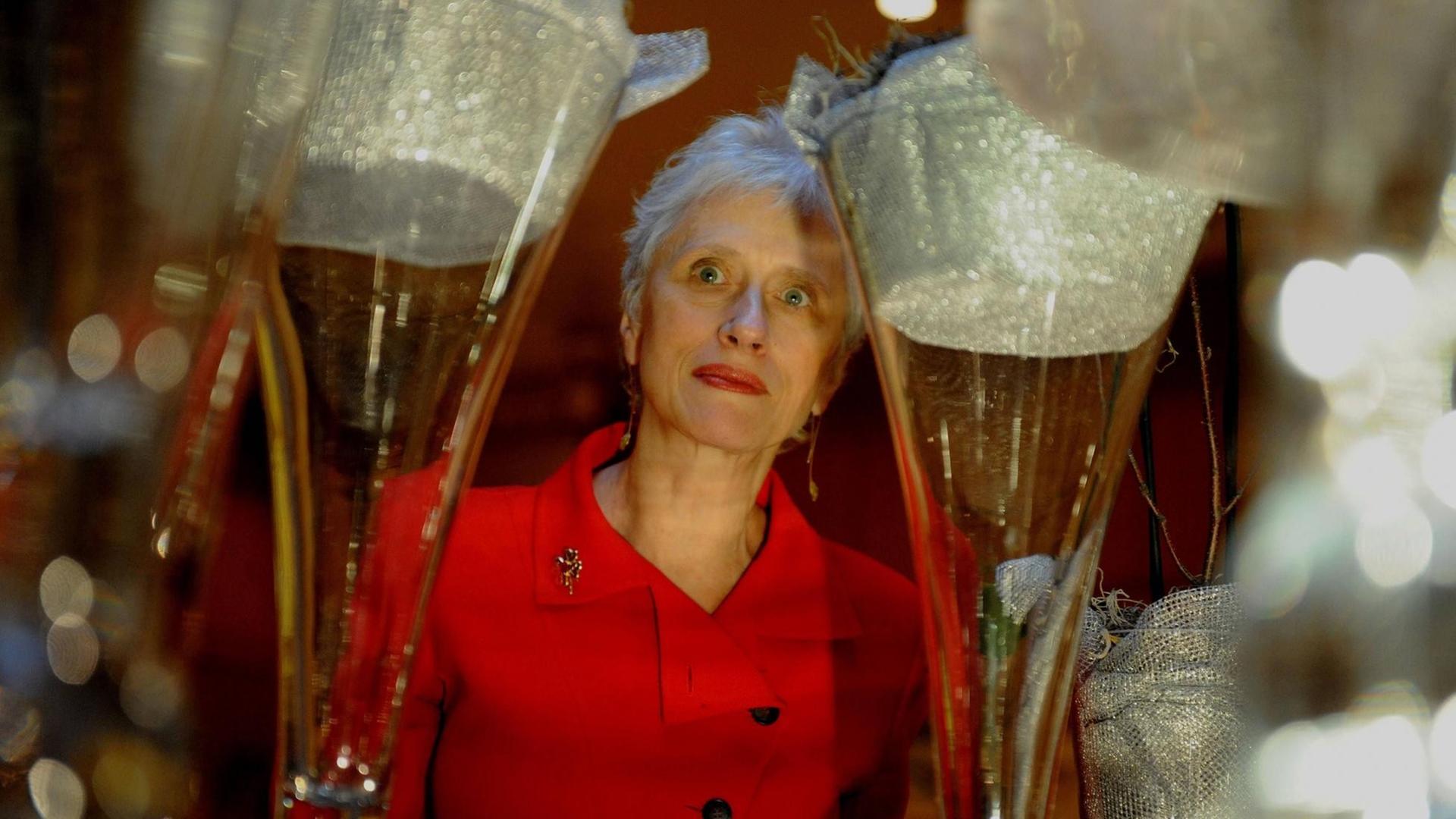 Schriftstellerin Sara Paretzky in rotem Kleid, im Vordergrund sehr groß zwei Sektgläser, in deren Mitte ist die Autorin zu sehen. Schriftstellerin Sara Paretzky in rotem Kleid, im Vordergrund sehr groß zwei Sektgläser, in deren Mitte ist die Autorin zu sehen.