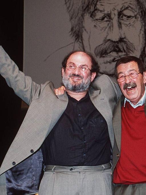 Salman Rushdie und Günter Grass stehen Arm in Arm auf einer Bühne und winken (1997)