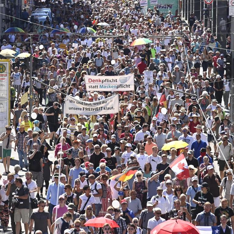 Eine Menschenmenge zieht durch eine Straße, auf einem Transparent steht: "Denkpflicht statt Maskenpflicht"