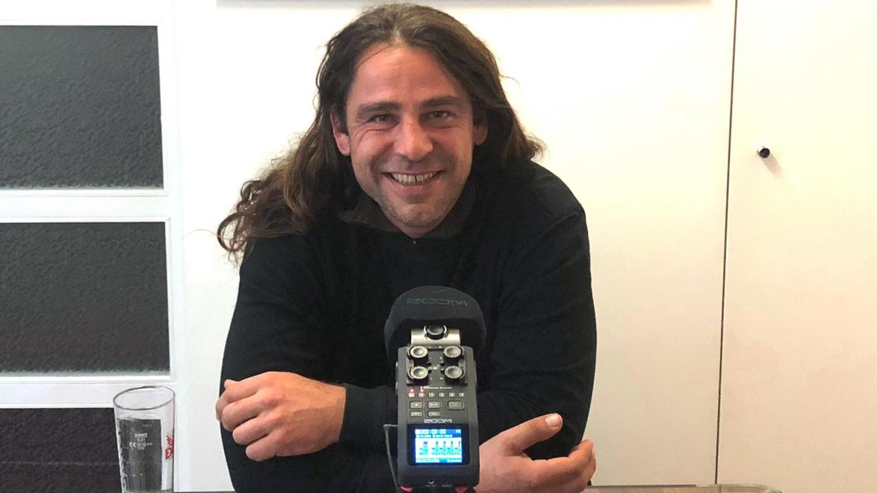 Ein Mann mit langen Haaren sitzt in einem Raum vor einem Mikrofon. Ein Mann mit langen Haaren sitzt in einem Raum vor einem Mikrofon.