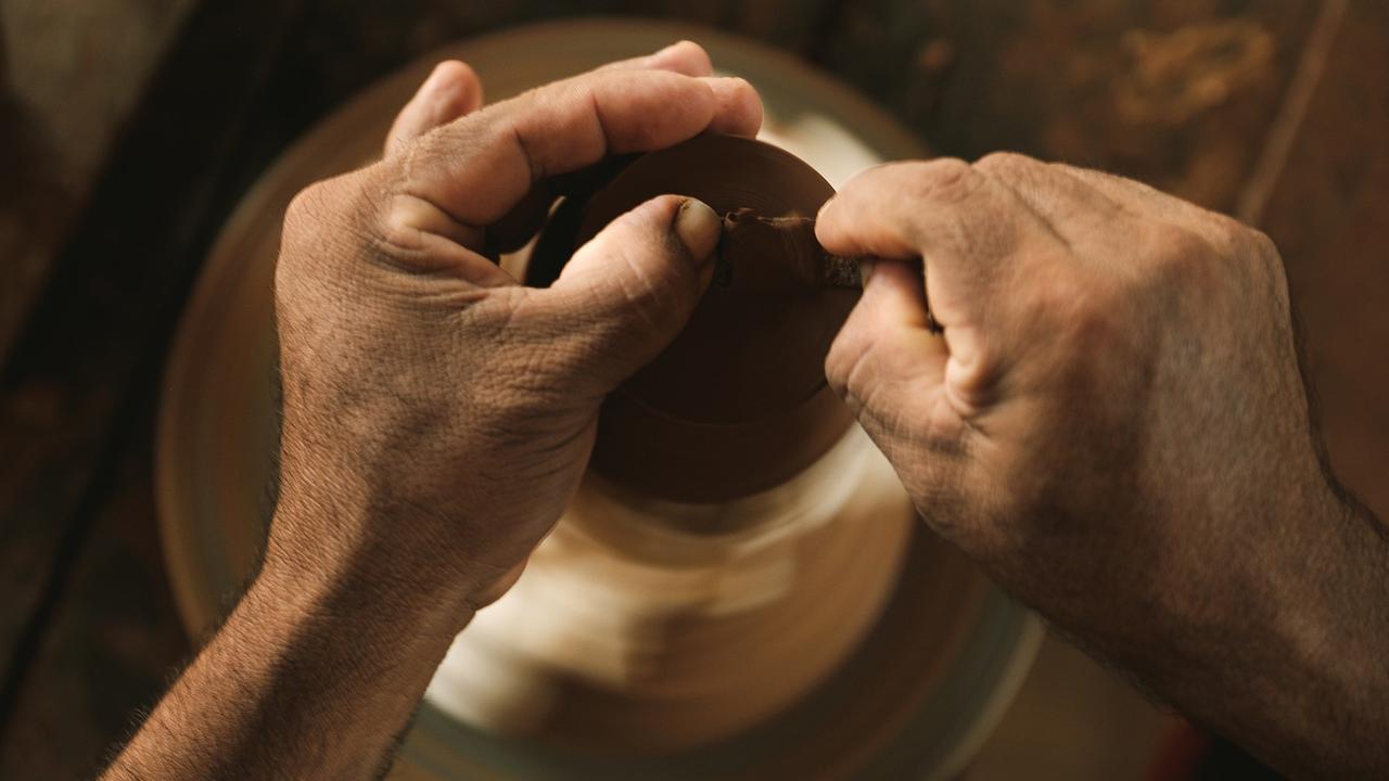 Hände formen auf einer Töpferscheibe eine Gefäß aus Ton.
