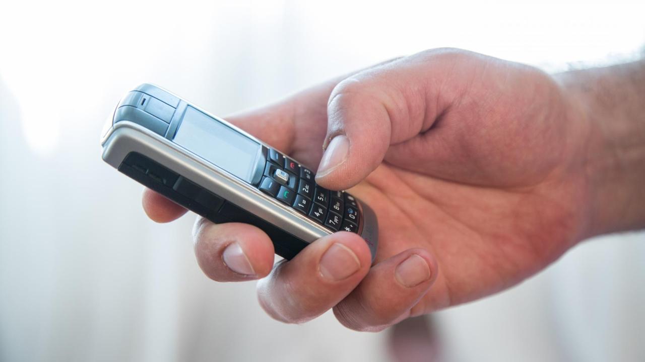 Die Hand eines Mannes hält ein altes Tastentelefon. Die Hand eines Mannes hält ein altes Tastentelefon.