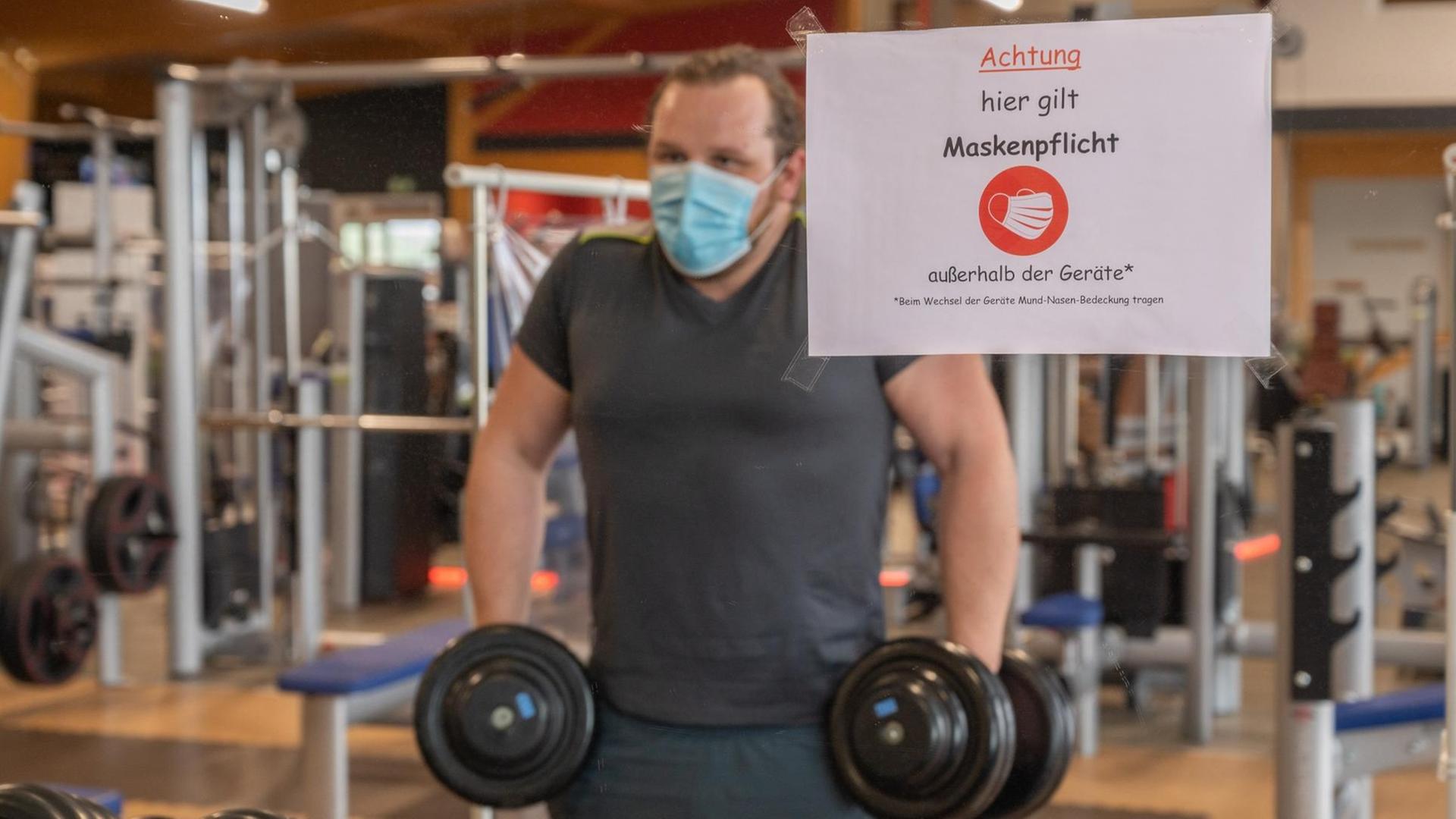 Ein Mann trainiert mit Mund-Nasen-Schutz in einem Fitnessstudio. Ein Mann trainiert mit Mund-Nasen-Schutz in einem Fitnessstudio.