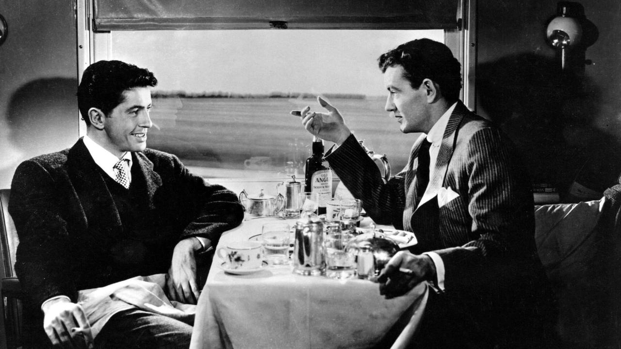 Zwei Männer sitzen in einem Zugabteil an einem Tisch.