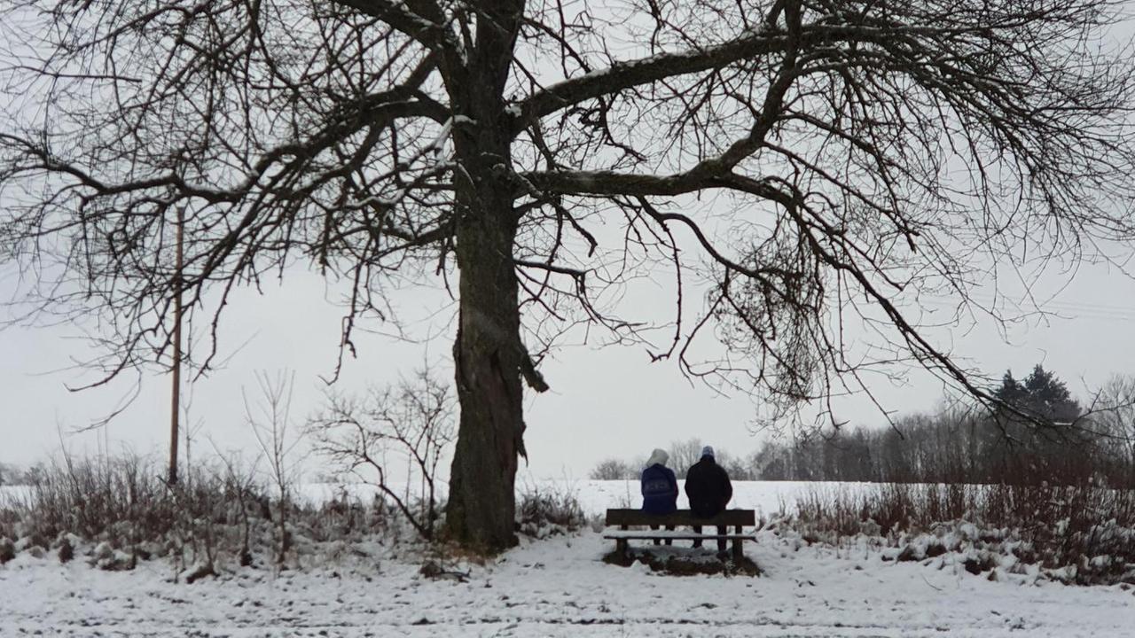 Ein Paar sitzt bei einem Spaziergang im Winter auf einer Bank. Ein Paar sitzt bei einem Spaziergang im Winter auf einer Bank.