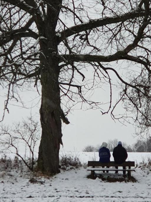 Ein Paar sitzt bei einem Spaziergang im Winter auf einer Bank.