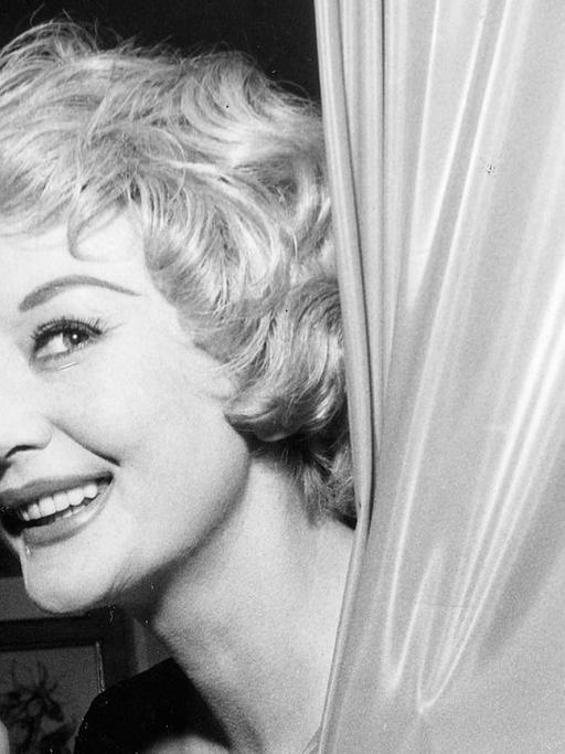 Die Sängerin Evelyn Künneke (*15.12.1921-28.04.2001). Sie lächelt frech zwischen einem Vorhang, 1959.
