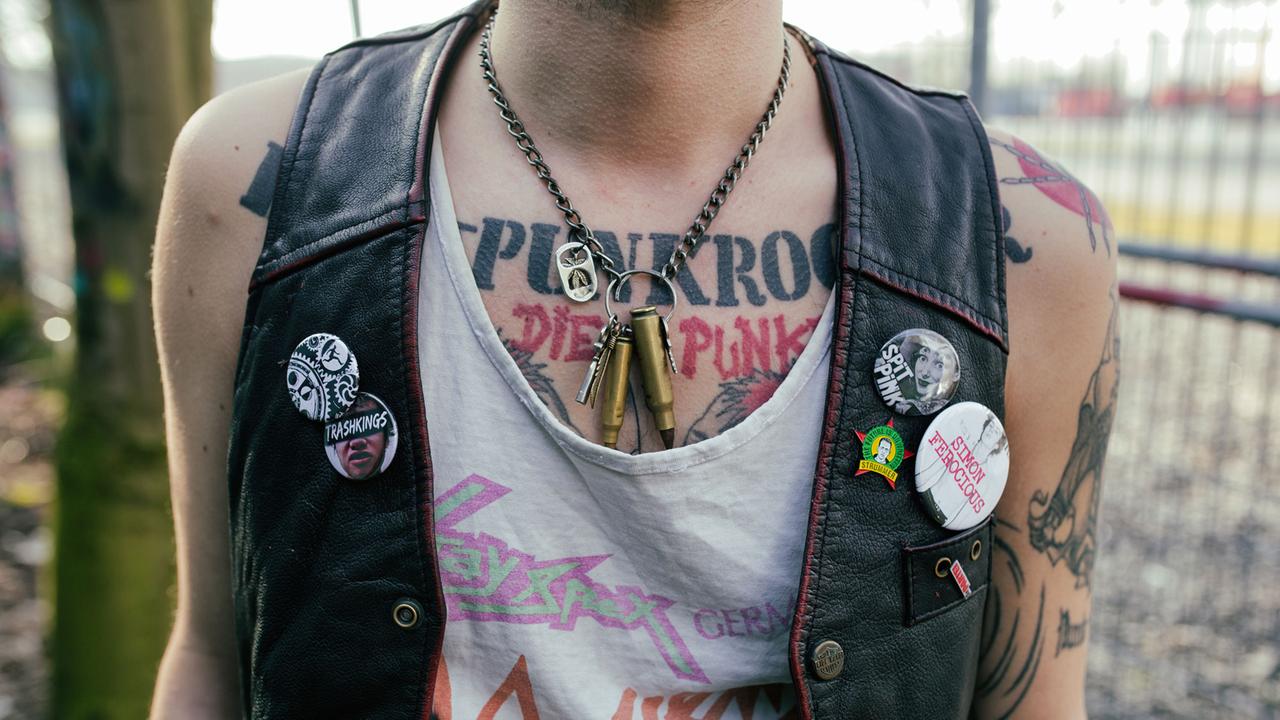 Ein Punk mit Lederweste und T-Shirt, die mit Buttons und Bemalungen verziert sind. Ein Punk mit Lederweste und T-Shirt, die mit Buttons und Bemalungen verziert sind.