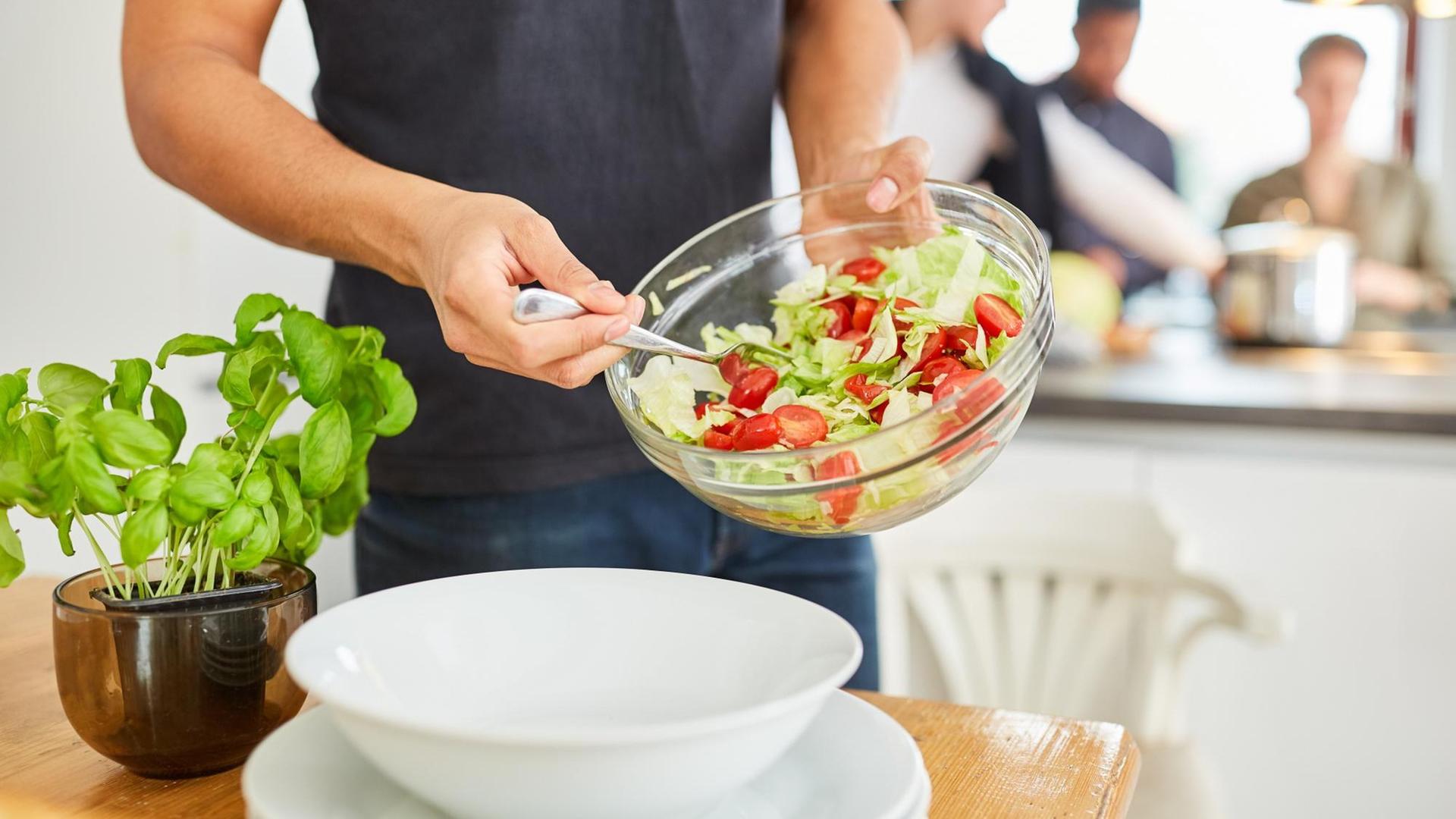 Mann mit Schüssel frischem Salat in Küche vor dem gemeinsamen Mittagessen in einer WG