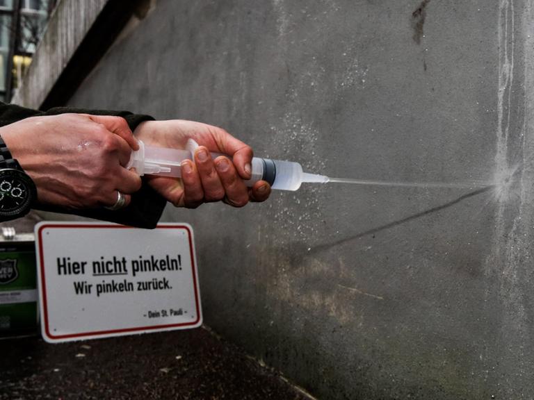 Die Quartiermanagerin der Reeperbahn, Julia Staron, demonstriert am 03.03.2015 in Hamburg im Stadtteil St. Pauli in der Einfahrt einer Tiefgarage neben einem Schild mit der Aufschrift "Hier nicht pinkeln! Wir pinkeln zurück" und einem Kanister mit superhydrophobem Lack die Reflexion von Flüssigkeit. Weil Betrunkene in dem legendären Stadtteil überall hinpinkeln, hat die Interessengemeinschaft St. Pauli Wände, an die in dem Viertel oft gepinkelt wird, mit superhydrophobem Lack beschichtet, der so wasserabweisend ist, dass der Urin regelrecht abprallt und zurückgespritzt wird.
