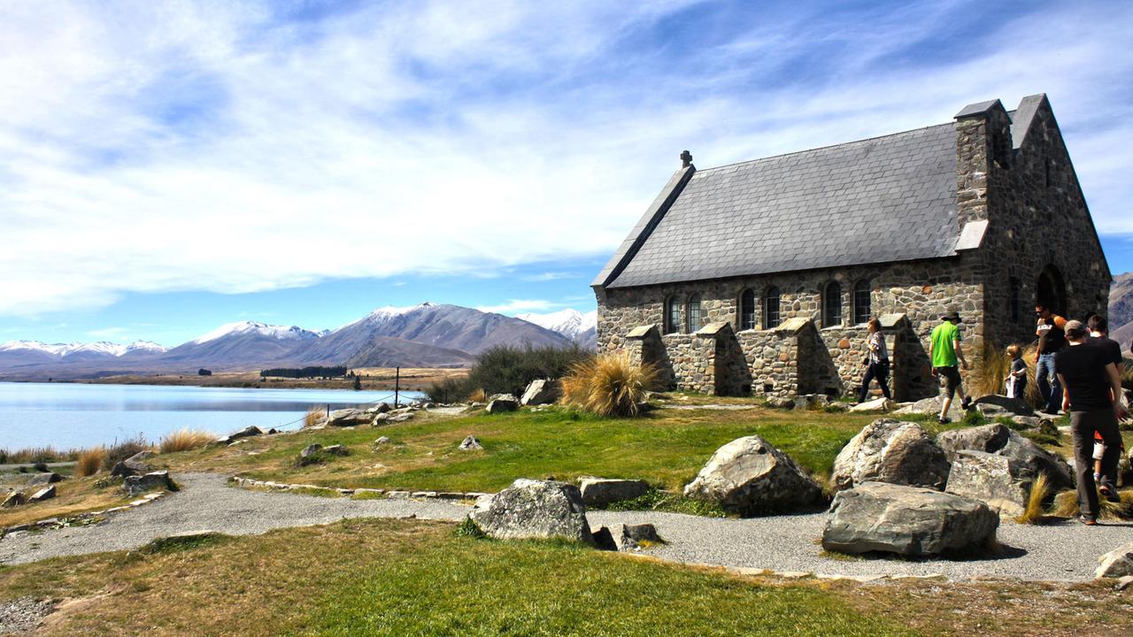 Touristen vor der Kirche des guten Hirten am Lake Tekapo. Im Hintergrund: Strahlend weißblauer Himmel und ein See. Touristen vor der Kirche des guten Hirten am Lake Tekapo. Im Hintergrund: Strahlend weißblauer Himmel und ein See.