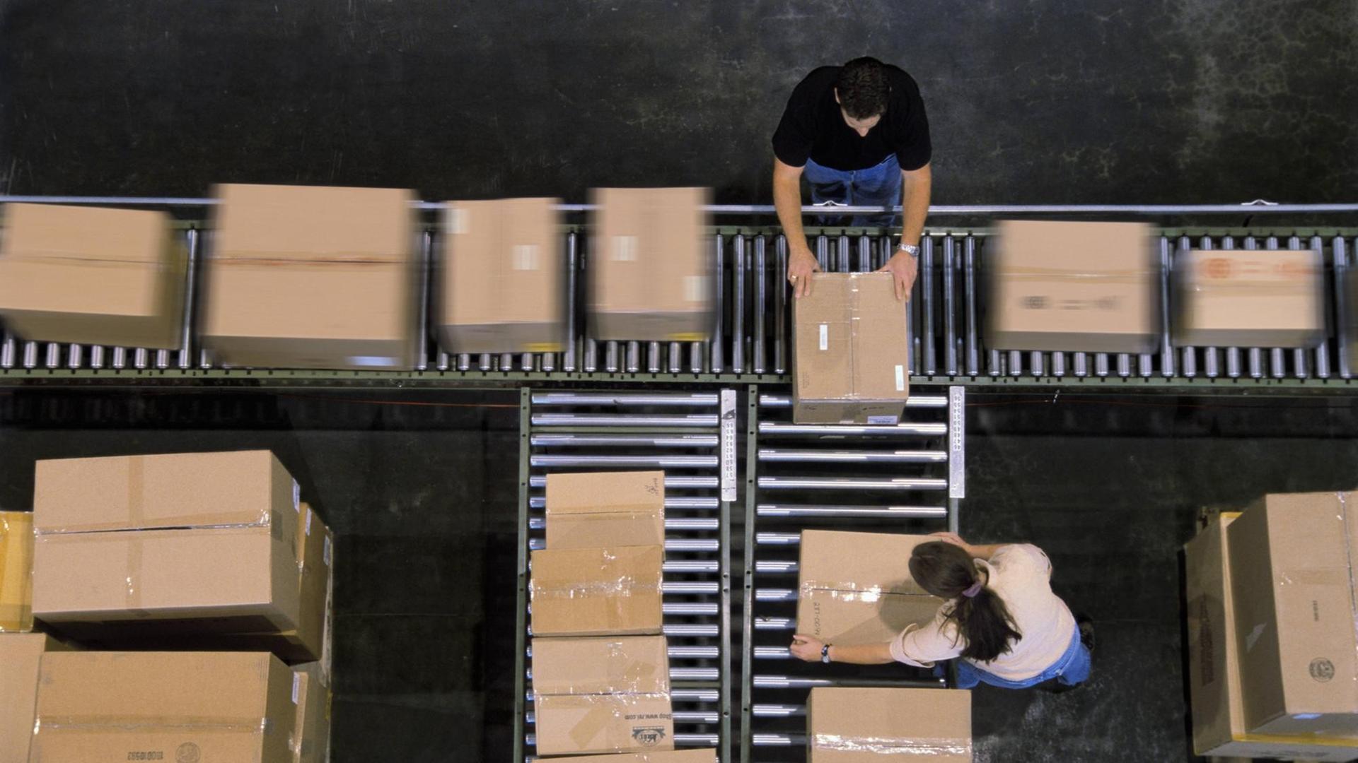 Mitarbeiter einer Lagerhalle sortieren Kartons auf einem Fließband in einem Verteilzentrum.