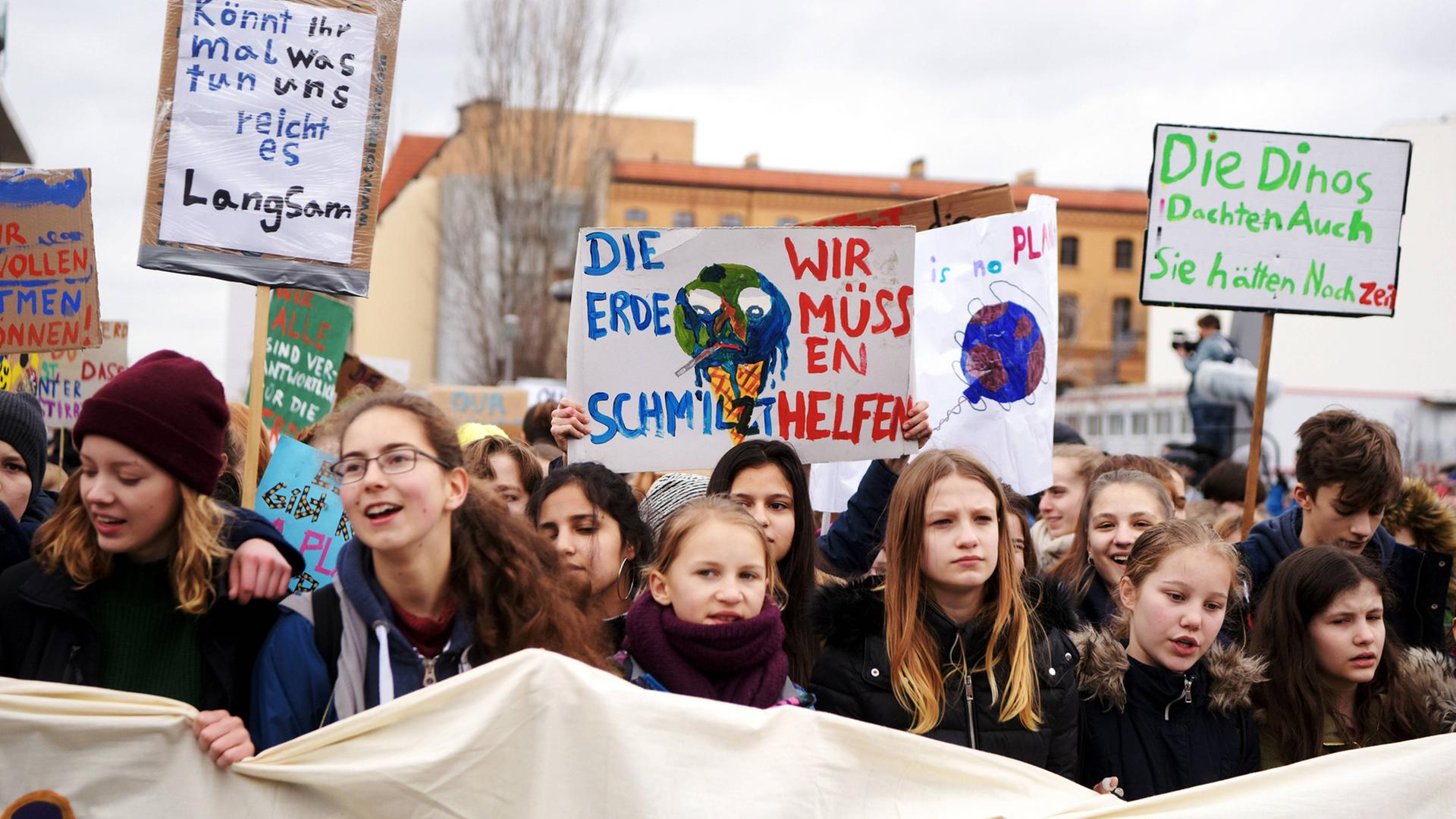 Eine Reihe Demonstrantinnen hält ein großes Banner und geht eine Straße entlang, sichtbar sind vor allem die Plakate, die sie in die Höhe halten. Unter anderem mit der Aufschrift "Die Erde schmilzt, wir müssen helfen". Eine Reihe Demonstrantinnen hält ein großes Banner und geht eine Straße entlang, sichtbar sind vor allem die Plakate, die sie in die Höhe halten. Unter anderem mit der Aufschrift "Die Erde schmilzt, wir müssen helfen".