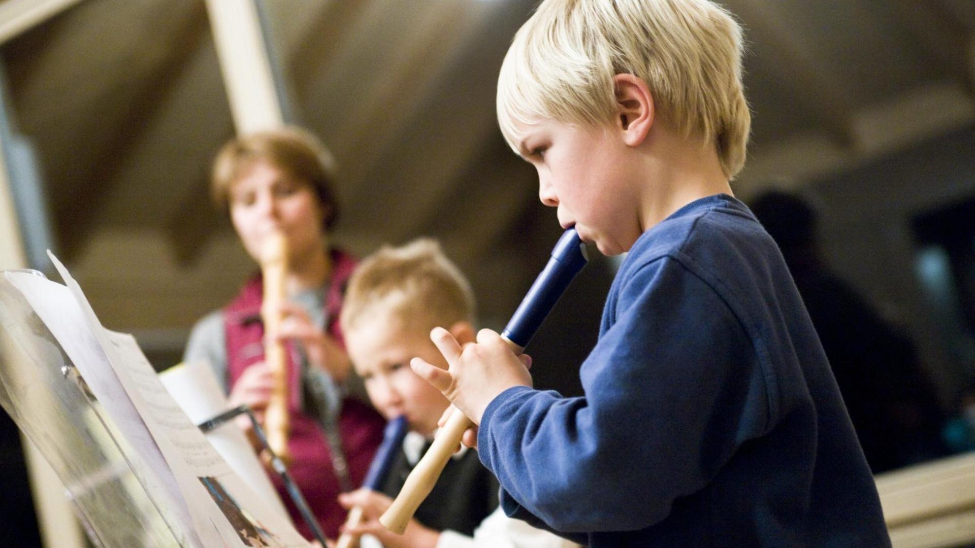 Drei Kinder spielen vor Notenständern auf ihren Blockflöten. Drei Kinder spielen vor Notenständern auf ihren Blockflöten.