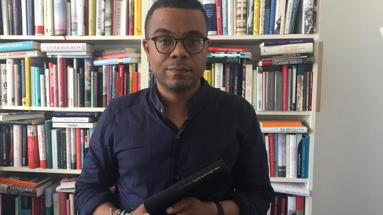 Der Literaturredakteur René Aguigah steht vor einem Bücherregal und hält ein Buch in der Hand.