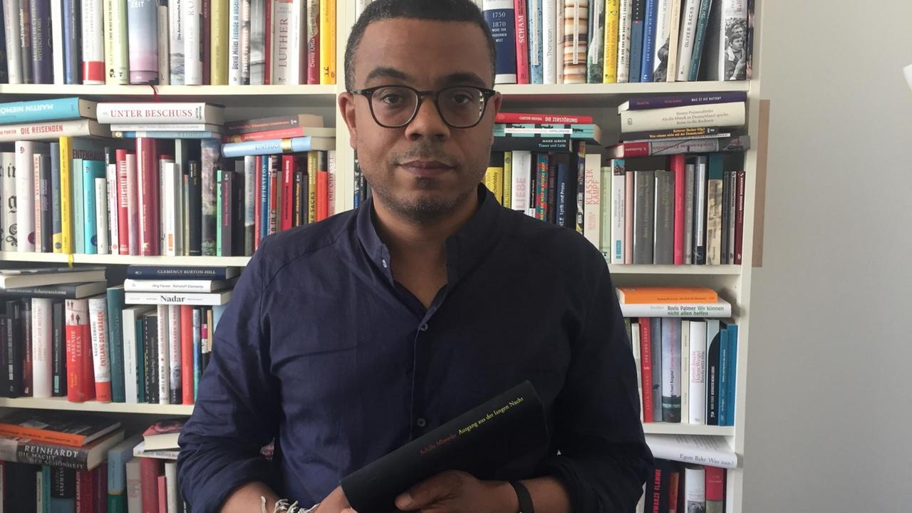 Der Literaturredakteur René Aguigah steht vor einem Bücherregal und hält ein Buch in der Hand. Der Literaturredakteur René Aguigah steht vor einem Bücherregal und hält ein Buch in der Hand.