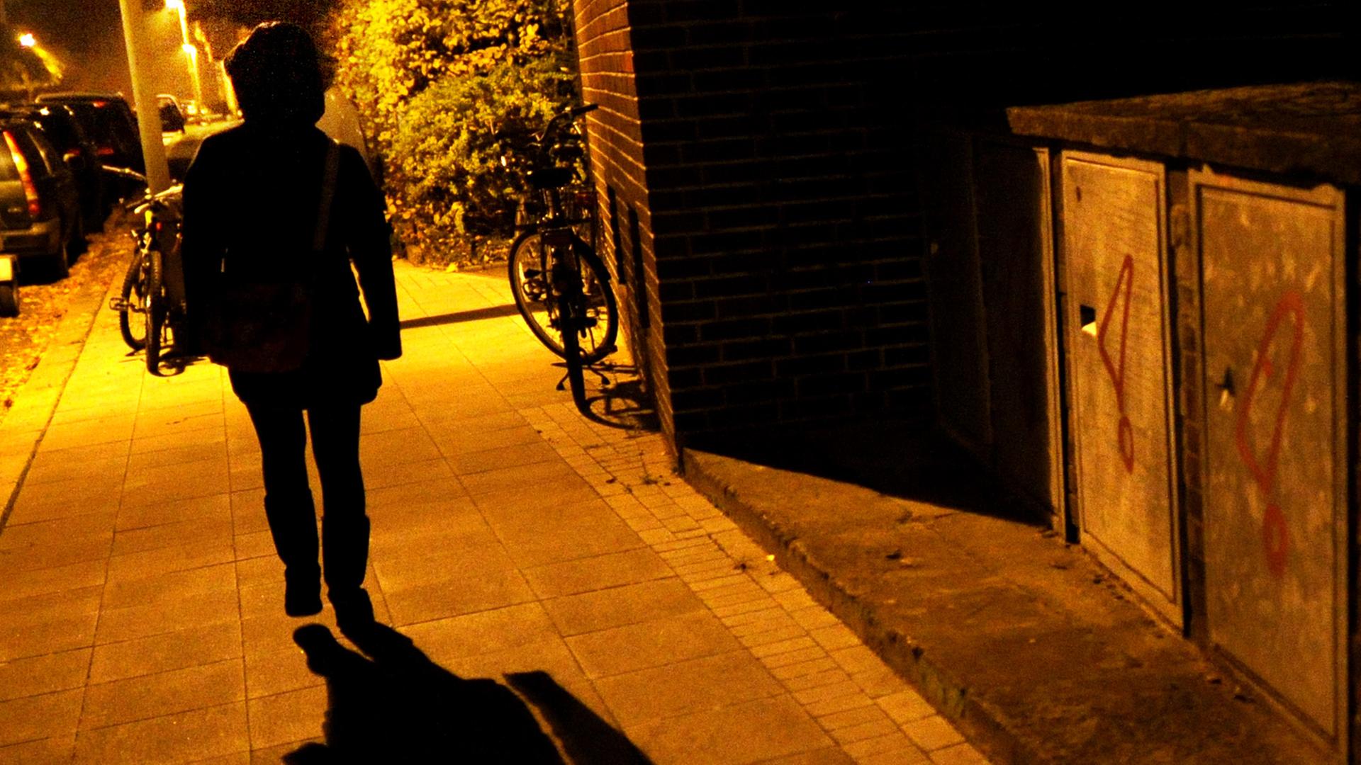 Eine Frau geht im Licht der Straßenlaternen alleine über eine dunkle Straße Eine Frau geht im Licht der Straßenlaternen alleine über eine dunkle Straße