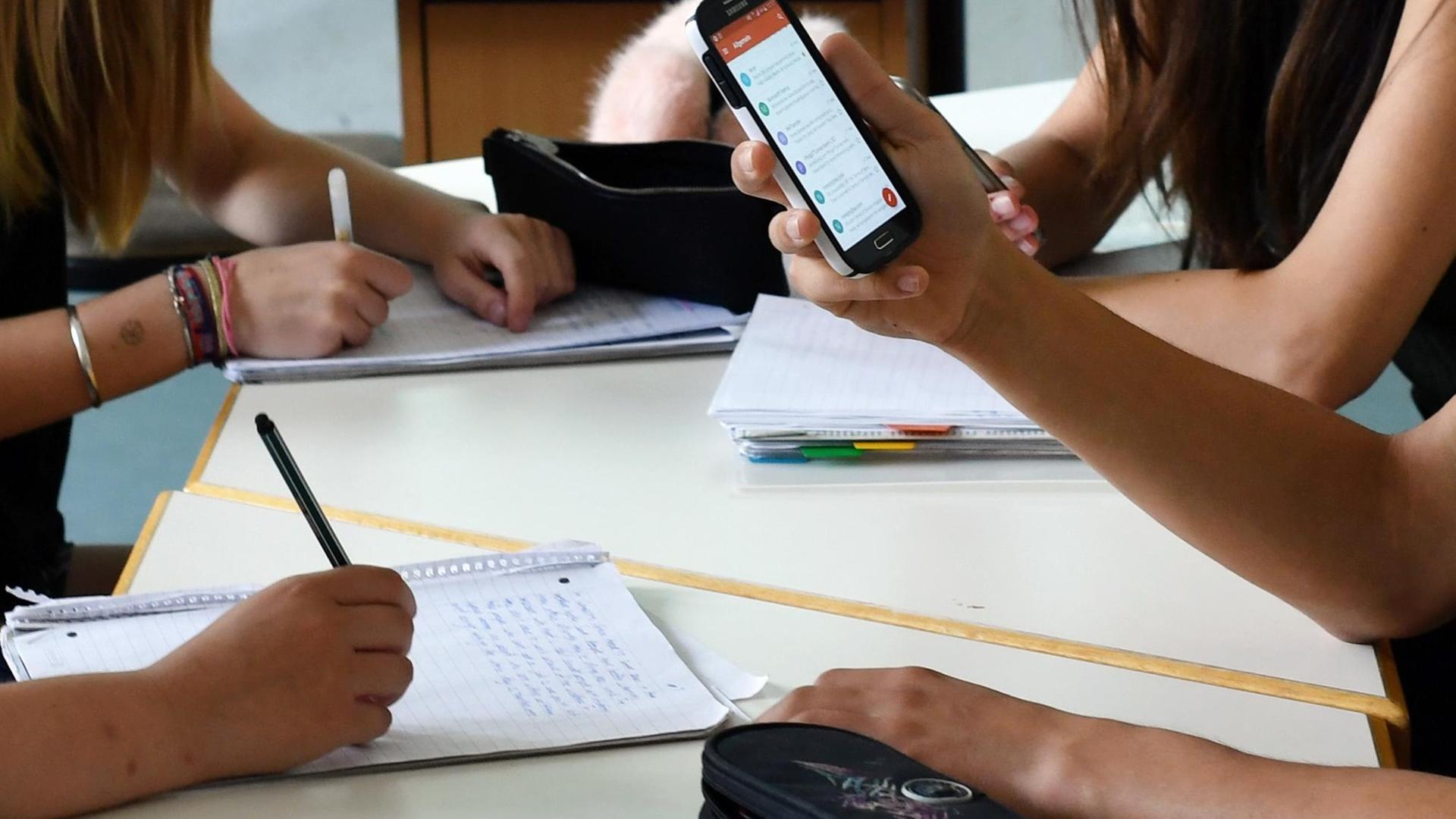 Schüler hält im Unterricht ein Handy in den Händen Schüler hält im Unterricht ein Handy in den Händen