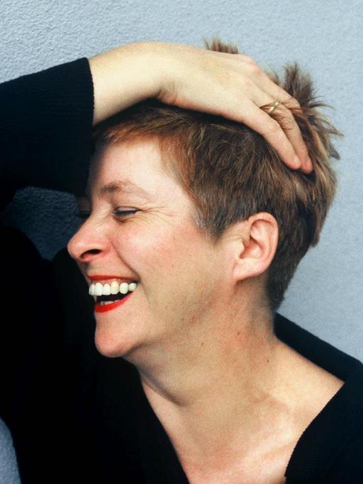 Lieselotte '' Pieke '' Biermann, deutsche Journalistin, Autorin und Uebersetzerin, rauft sich lachend die Haare vor einer blauen Hauswand.