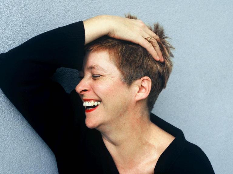 Lieselotte '' Pieke '' Biermann, deutsche Journalistin, Autorin und Uebersetzerin, rauft sich lachend die Haare vor einer blauen Hauswand.